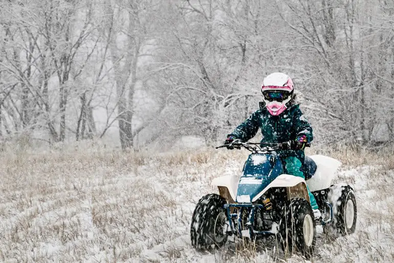 kid wearing ATV helmet riding 4 wheeler in winter