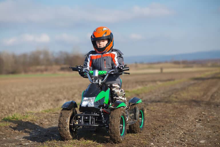 little boy in orange helmet riding green ATV