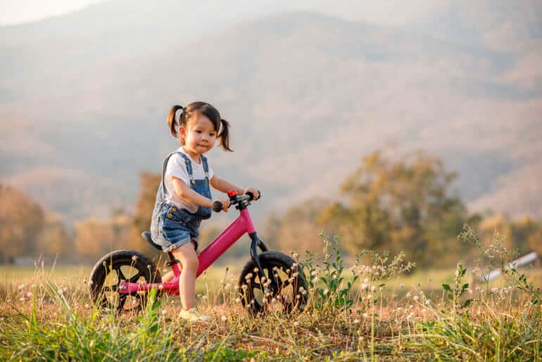 little girl riding pink bike in field